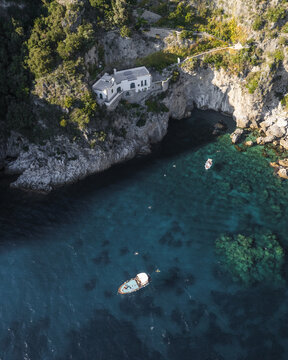 Aerial view of a white villa perched dramatically on rugged cliffs overlooking the turquoise waters of the Amalfi Coast, Conca dei Marini, Campania, Italy.