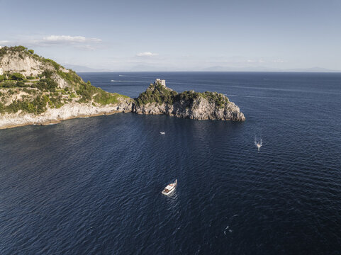 Aerial view of azure waters meet rugged cliffs and a historic tower stands guard, boats dotting the seascape, Conca dei Marini, Amalfi Coast, Campania, Italy.