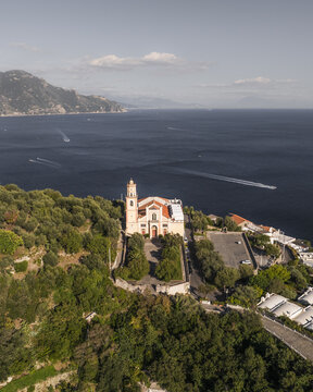 Aerial view of the historic church perched atop a cliff overlooking the deep blue sea, framed by lush greenery, Conca dei Marini, Amalfi Coast, Campania, Italy.
