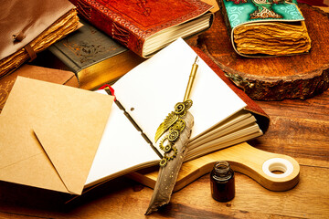 A creative artistic still life composition featuring multiple vintage journals, an open blank notebook, a decorative steampunk feather pen, kraft paper envelope, and an ink bottle 