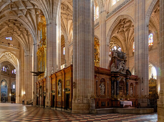 The Segovia Cathedral interior showcases towering Gothic arches and an ornate vaulted ceiling. Massive columns frame the central altarpiece and detailed stained glass