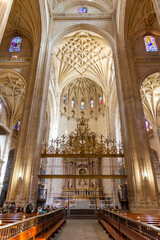 Obraz premium The Segovia Cathedral interior showcases towering Gothic arches and an ornate vaulted ceiling. Massive columns frame the central altarpiece and detailed stained glass