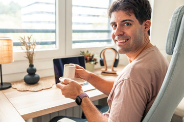 Young man teleworking from home smiling and drinking coffee