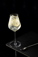 A sophisticated cocktail served in a tall stemmed glass, ice cubes glistening, garnished with a bright lemon wheel. Ideal for bar, mixology, or luxury lifestyle photography on black backdrop.