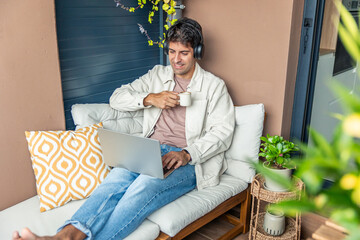 Young Hispanic man teleworking from home on balcony enjoying coffee