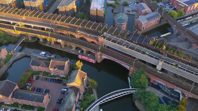 Top-down sunrise aerial video of Manchester&rsquo;s Castlefield viaducts showing trams, a train, and canal boats along Bridgewater Canal.