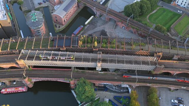 Top-down sunrise aerial video of Manchester&rsquo;s Castlefield viaducts showing trams, a train, and canal boats along Bridgewater Canal.