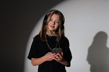Young caucasian girl with headphones listening to music on smartphone in shadowy room