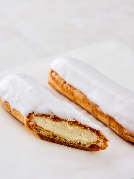 A creamy pastry filled with rich filling is cut in half, revealing its soft texture. The pastry is covered with a glossy white icing. It is placed on a simple white background
