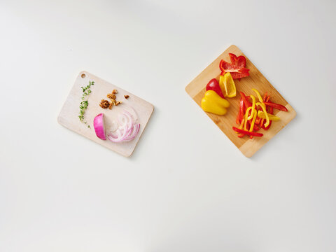 Colorful peppers and onions are neatly arranged on wooden cutting boards in a clean kitchen. Fresh herbs are also visible, ready for cooking