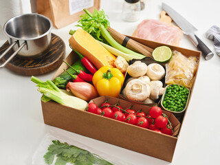 A variety of fresh vegetables, including tomatoes, peppers, and mushrooms, are arranged in a box on a kitchen counter. Ingredients are ready for a nutritious dish preparation