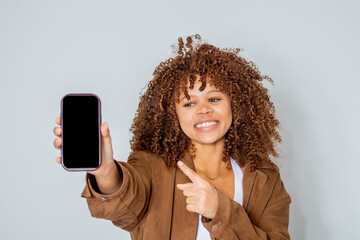smiling beautiful young latina woman with afro hair isolated pointing and showing mobile phone