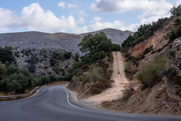 Beautiful panoramic view of the Cretan countryside with mountains, green valleys, olive groves, and a small traditional village under a bright blue sky with scattered clouds. Captured on a sunny day