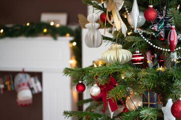 Decorated Christmas tree, real Nordmann fir in front of blurred living room furniture. Macro photography shows Christmas tree ornaments made of honeycomb paper and baubles in red, white, and champagne