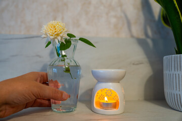 An aroma lamp with essential oil and a beautiful vanilla-colored tea rose in an elegant glass vase.