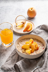 Oatmeal with peaches and nuts  in a bowl on a light background with honey