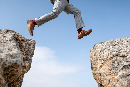 Close up, A businessman leaping from one cliff to another, concept of risk - Powered by Adobe