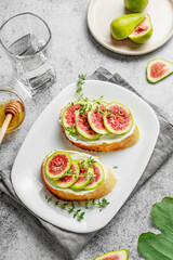 Sweet toasts with fresh figs, cheese, thyme, and honey on a gray background.