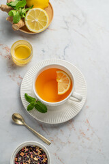 Tea with lemon, ginger, honey, and mint in a cup on a marble background with citrus fruits