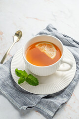 Hot tea with lemon and mint in a cup on a marble background with spoon and napkin.