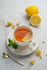 Tea with lemon and mint in a cup on a marble background with citrus fruits and dry flowers.