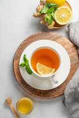 Tea with lemon, ginger, honey, and mint in a cup on a light background with citrus fruits