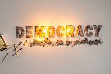 The word democracy burns on white seamless background