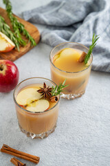 Two glasses of apple cider with cinnamon, anise, and rosemary on a light background with fresh fruits