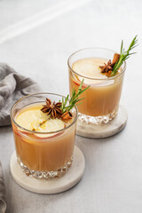 Two glasses of apple cider with cinnamon, anise, and rosemary on a light background with sunlight