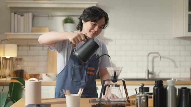 Asian Chinese male barista prepares filter coffee at home bar counter, young adult freelancer feeling relaxed while brewing specialty coffee during work break, enjoying peaceful coffee-making ritual