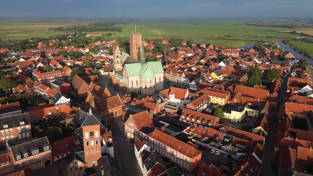 Aerial view of Ribe Cathedral in Denmark, showcasing medieval architecture, red rooftops, and scenic countryside in soft daylight