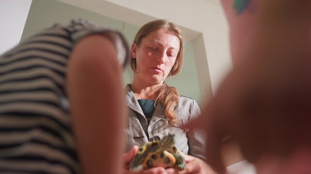 Close up of teacher holding tortoise while explaining behavior to children gathered nearby, educational moment focused on interaction with reptile encouraging observation