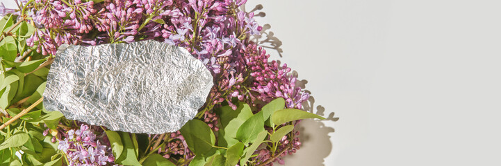 Crumpled foil on purple lilac flowers and green leaves with light grey background.