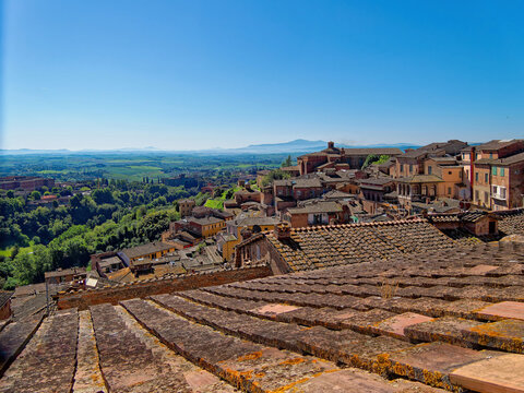 A sweeping Tuscan panorama where Siena&rsquo;s terracotta rooftops meet verdant hills and a distant mountain under a radiant sky. Travel to Italy.