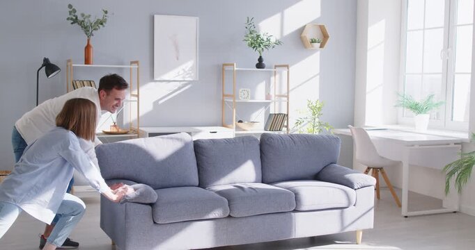 Happy family couple moving sofa to their new house. Smiling husband and wife working together, giving each other high five, feeling excited and full of energy, arranging furniture in bright new home.