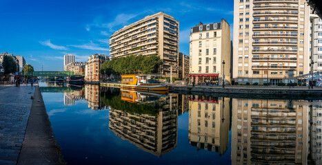 Paris, France - 10 11 2025: Ourcq Canal. Panoramic view of a colorful touristic boats, people walking, buildings and bridges reflecting on the water