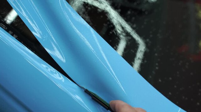 Precision cutting of PPF wrap on car body 4k video. Precision PPF wrapping and detailing on car panel using sharp blade to trim wrap with accuracy. Car detailing involves vinyl cutting techniques.