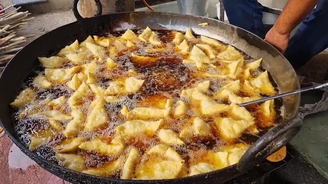 close up shot of Kachori Samosa frying in huge pan filled with hot black oil showing the popularity of this spicy savory street food snack in north India and the unhealthy food they consume