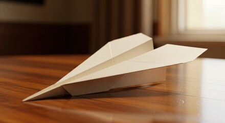 White paper airplane resting on a shiny wooden table indoors during daytime, symbolizing childhood dreams and imagination