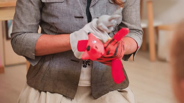 Close up of adult using glove puppets to entertain children, moving toys gently and encouraging attention, laughter, and speech during classroom session, warm learning mood
