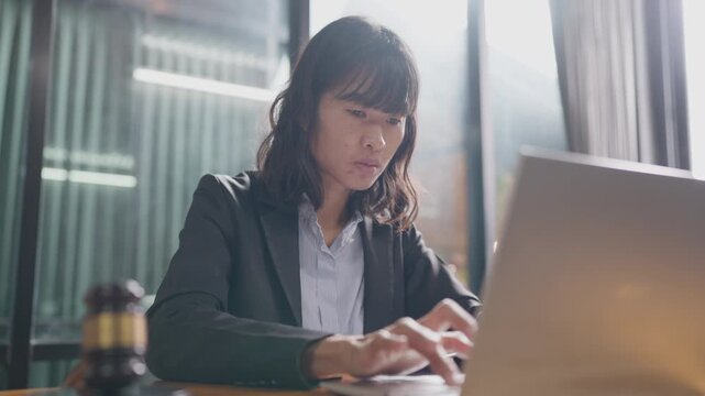 Professional Asian female lawyer working on a laptop at her desk with gavel on table. Legal profession and justice concept.