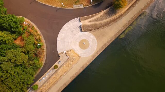 Person wearing white clothes lies in the circle center drawn at the quay of the river. Top view on the waterfront of the Allegheny River in Pittsburg, Pennsylvania, USA.