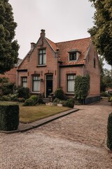 A charming brick house featuring a beautifully landscaped garden, complemented by a quaint cobblestone driveway, nestled in a serene neighborhood under overcast skies