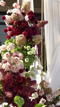 Colorful wedding romantic flower arch with white fabric. Summer atmosphere on the street. Green white and red flowers. Rose, hydrangea, anthurium, dahlia, chrysanthemum, amaranth, dianthus white spray