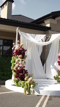 Colorful wedding romantic flower arch with white fabric. Summer atmosphere on the street. Green white and red flowers. Rose, hydrangea, anthurium, dahlia, chrysanthemum, amaranth, dianthus white spray