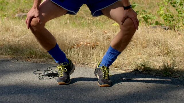 A dedicated runner pauses on the path, resting their knees in snug blue compression socks, either preparing for intense exercise or recovering after a challenging workout