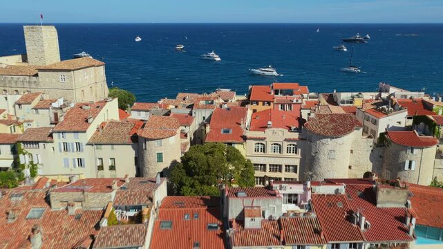 Aerial drone view of Antibes Old Town rooftops, Chateau Grimaldi, and stone ramparts overlooking the deep blue Mediterranean