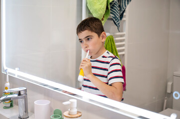 Young boy brushing his teeth with electric toothbrush in home bathroom mirror