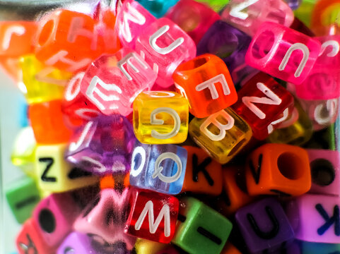 Multicolored alphabet beads with letters on each face are scattered.  - Powered by Adobe