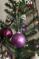 A close-up of a purple glittery Christmas ornament hanging from a decorated evergreen tree